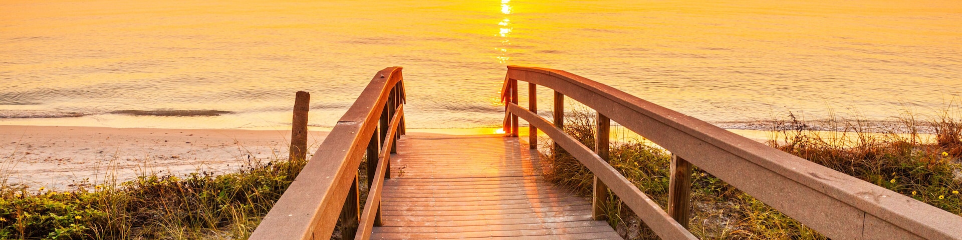 Pasarela de madera que lleva a una playa al atardecer.
