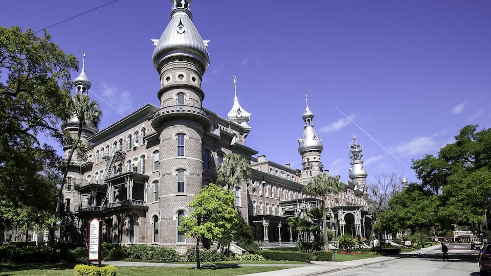 A large, ornate building with multiple domes and towers, surrounded by trees and a clear blue sky.