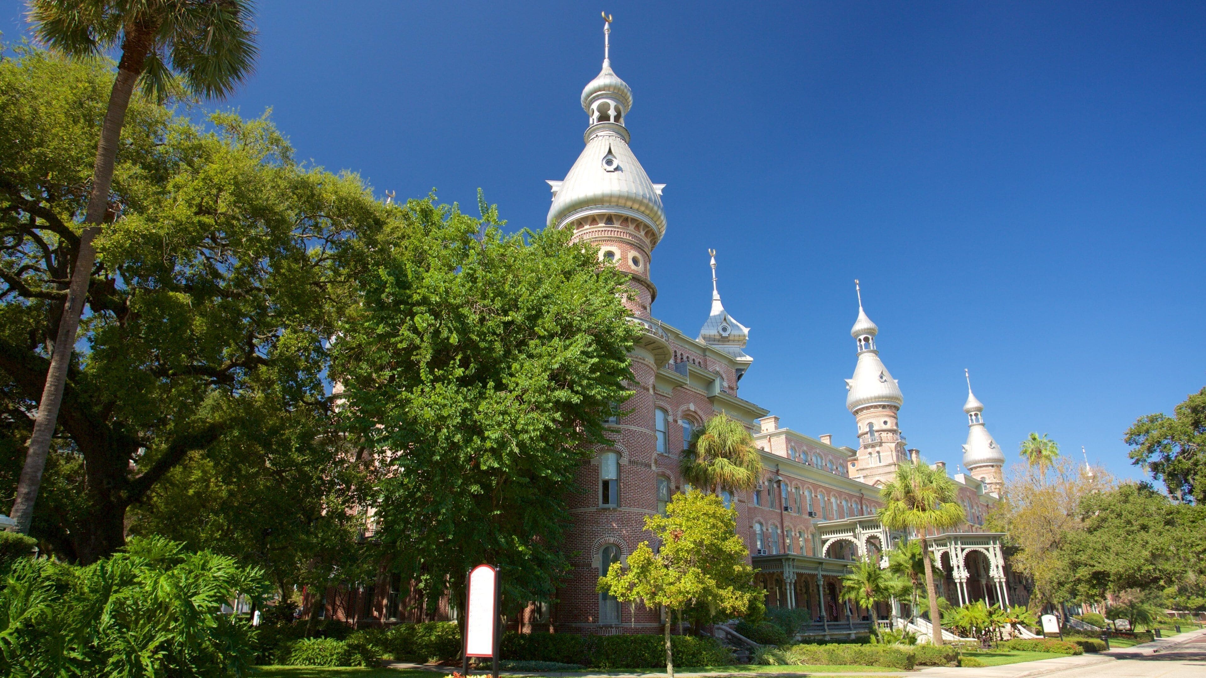 A grand building with multiple domes and spires, surrounded by lush greenery and palm trees.