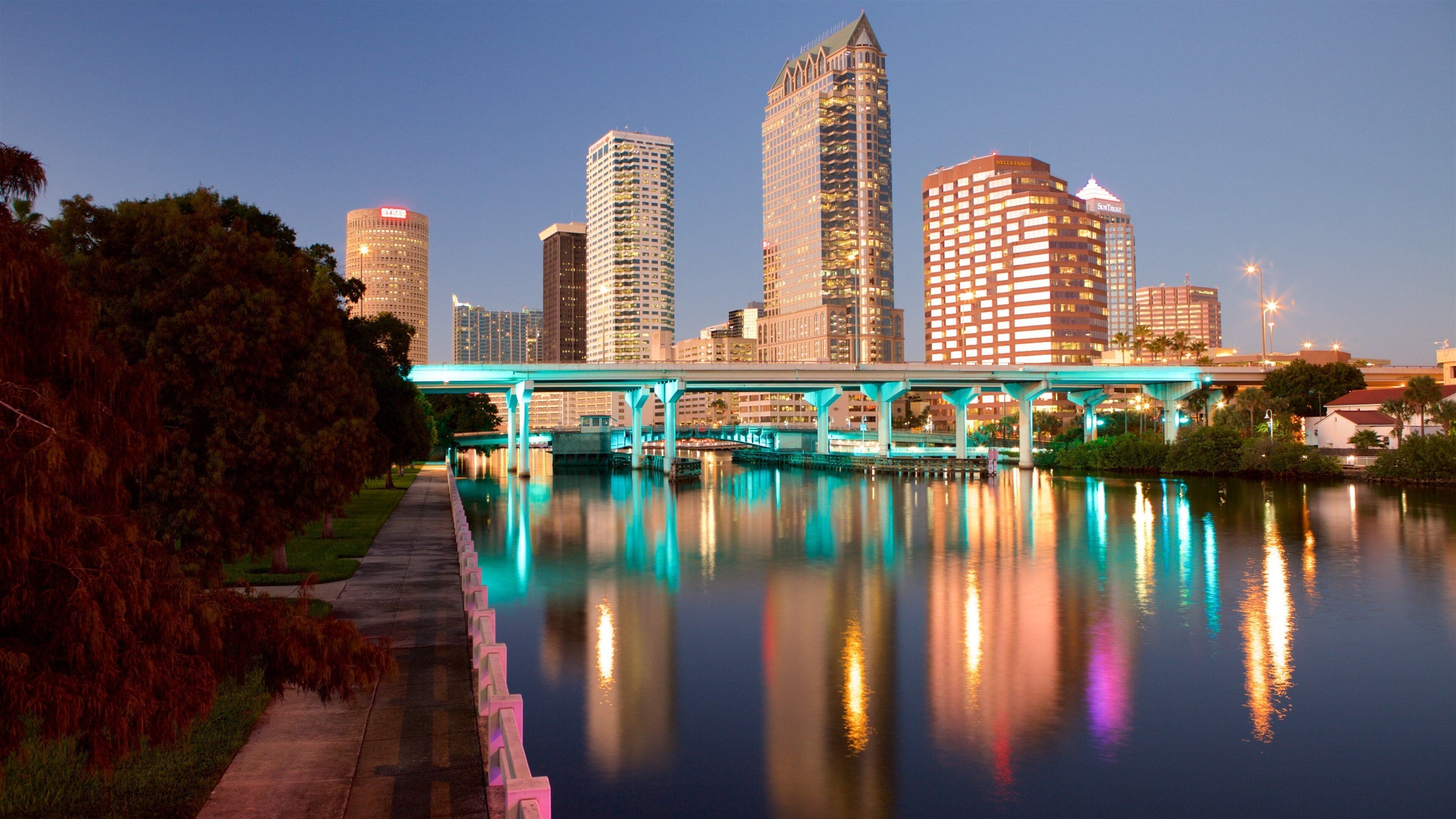 A city skyline with a bridge over a calm river, reflecting the buildings and lights.