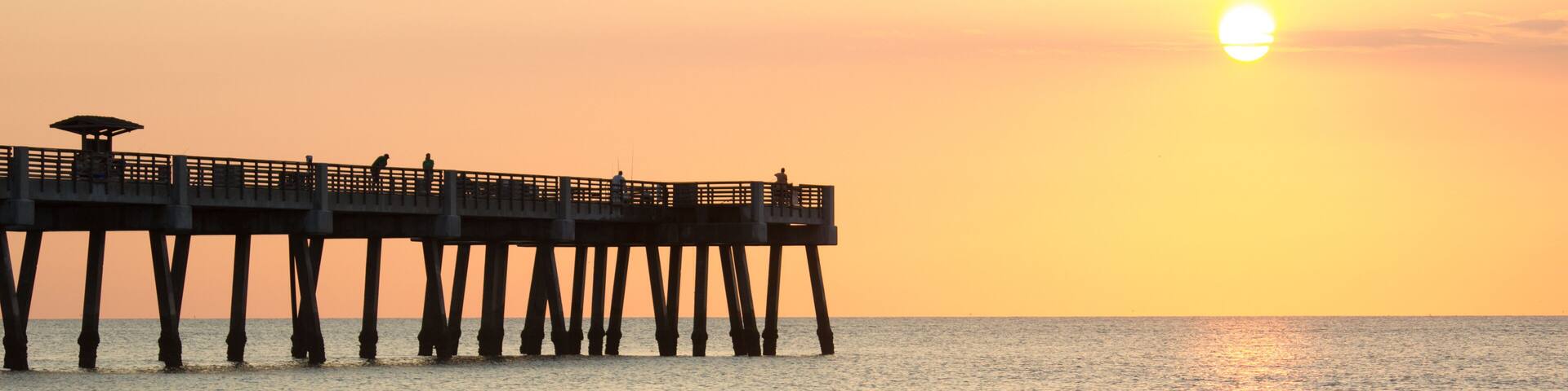 A sunset over the ocean with a pier extending into the water.