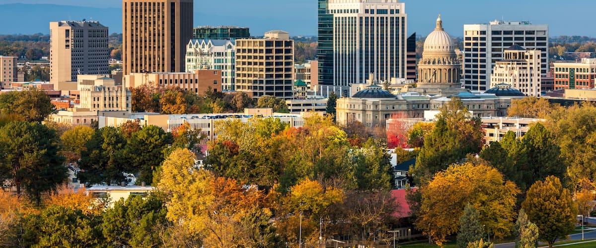 A city skyline with modern and historic buildings, surrounded by autumn-colored trees.