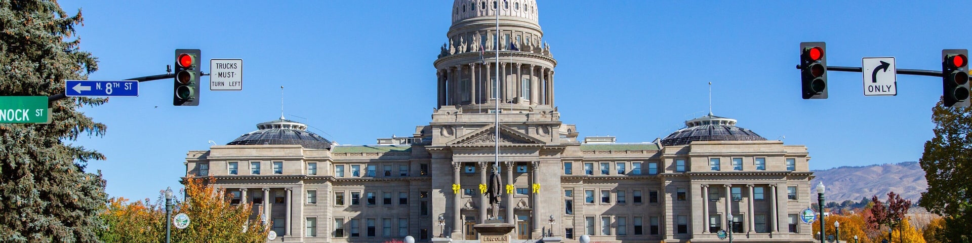 A large neoclassical building with a prominent dome, situated at a street intersection with traffic lights and street signs.