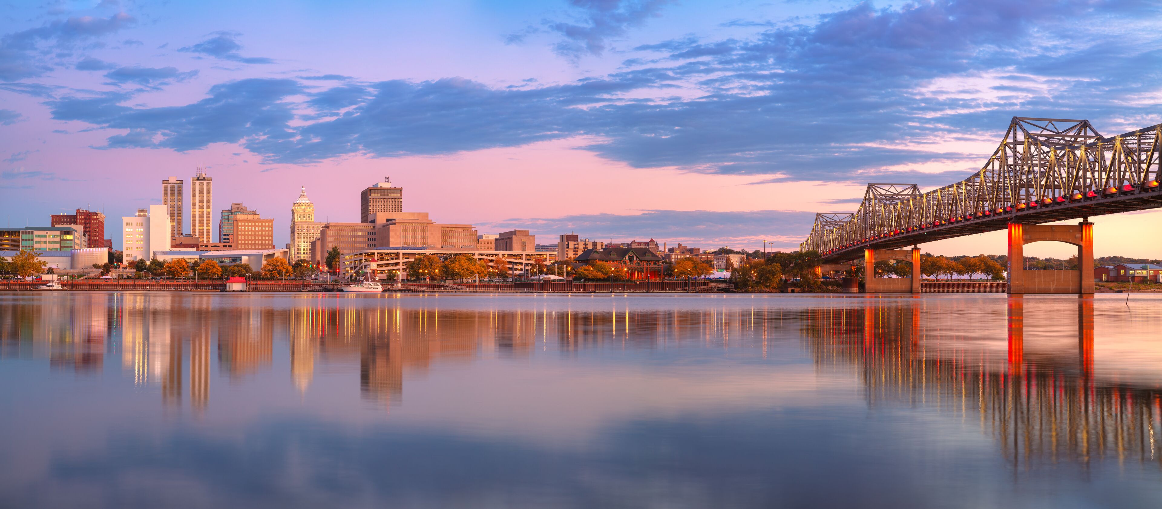 A city skyline with a bridge over a calm river reflecting the buildings.