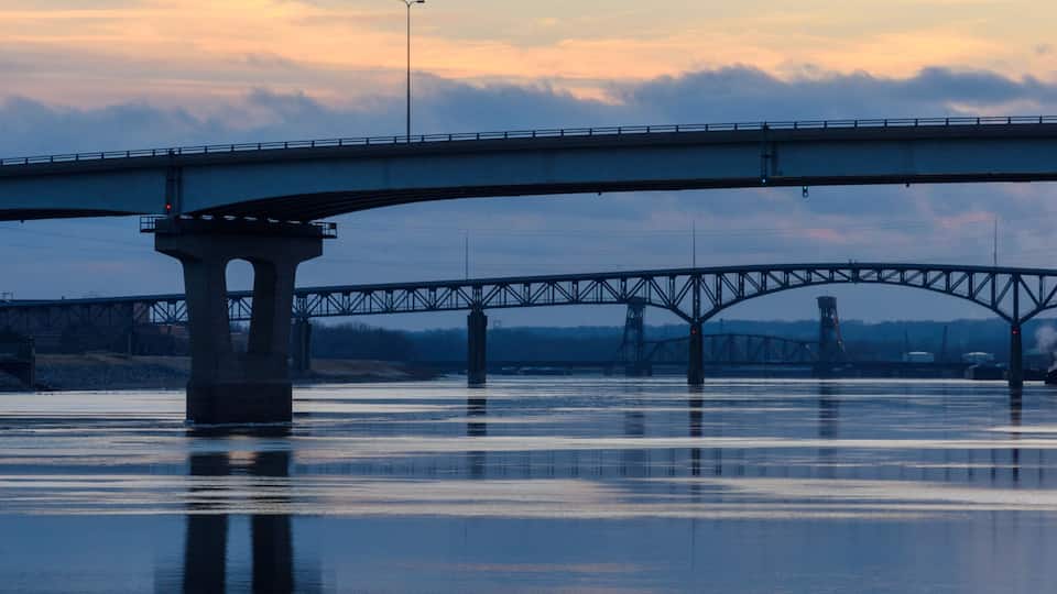 A bridge over calm water with a sunset sky.