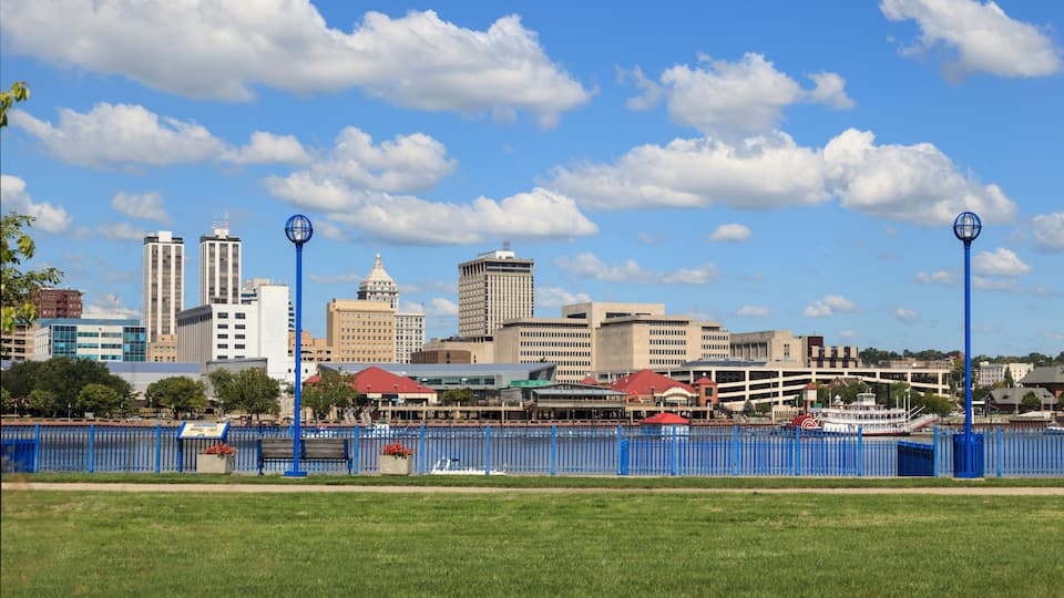 A city skyline with prominent buildings, a river, and a blue fence.