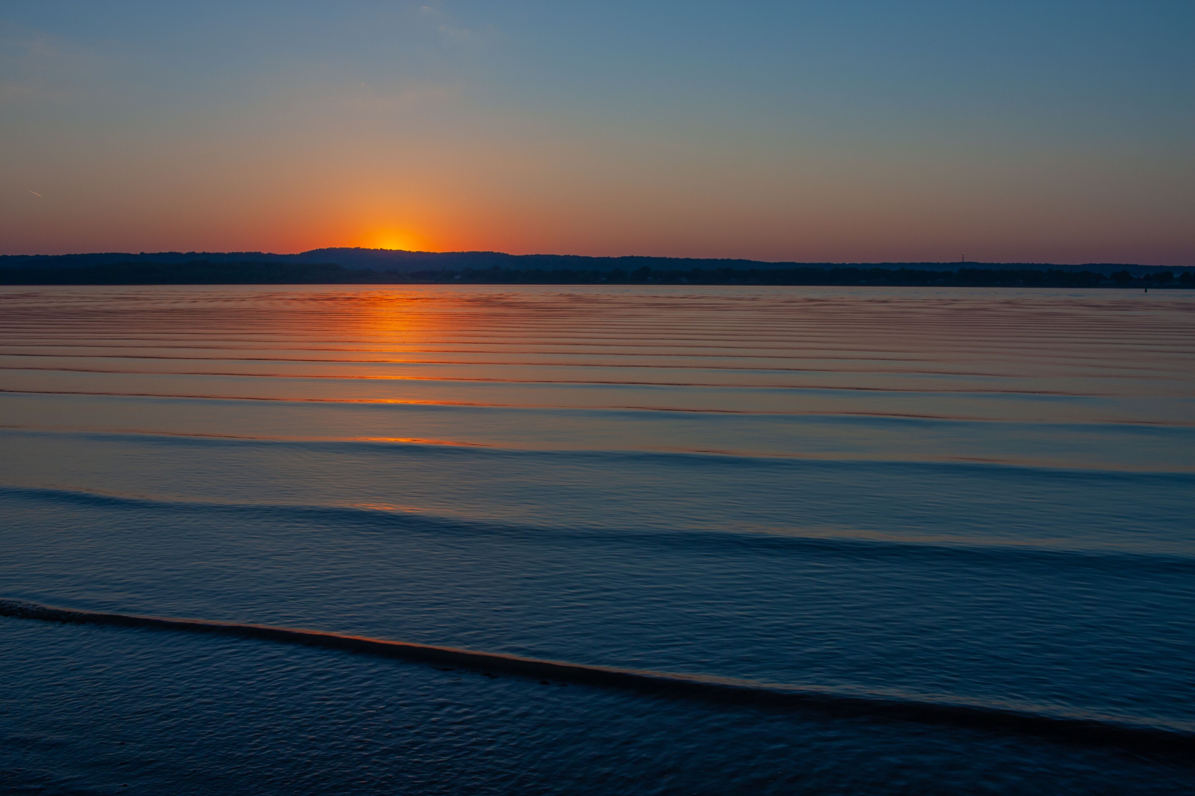 Un atardecer sobre aguas tranquilas con una costa lejana.