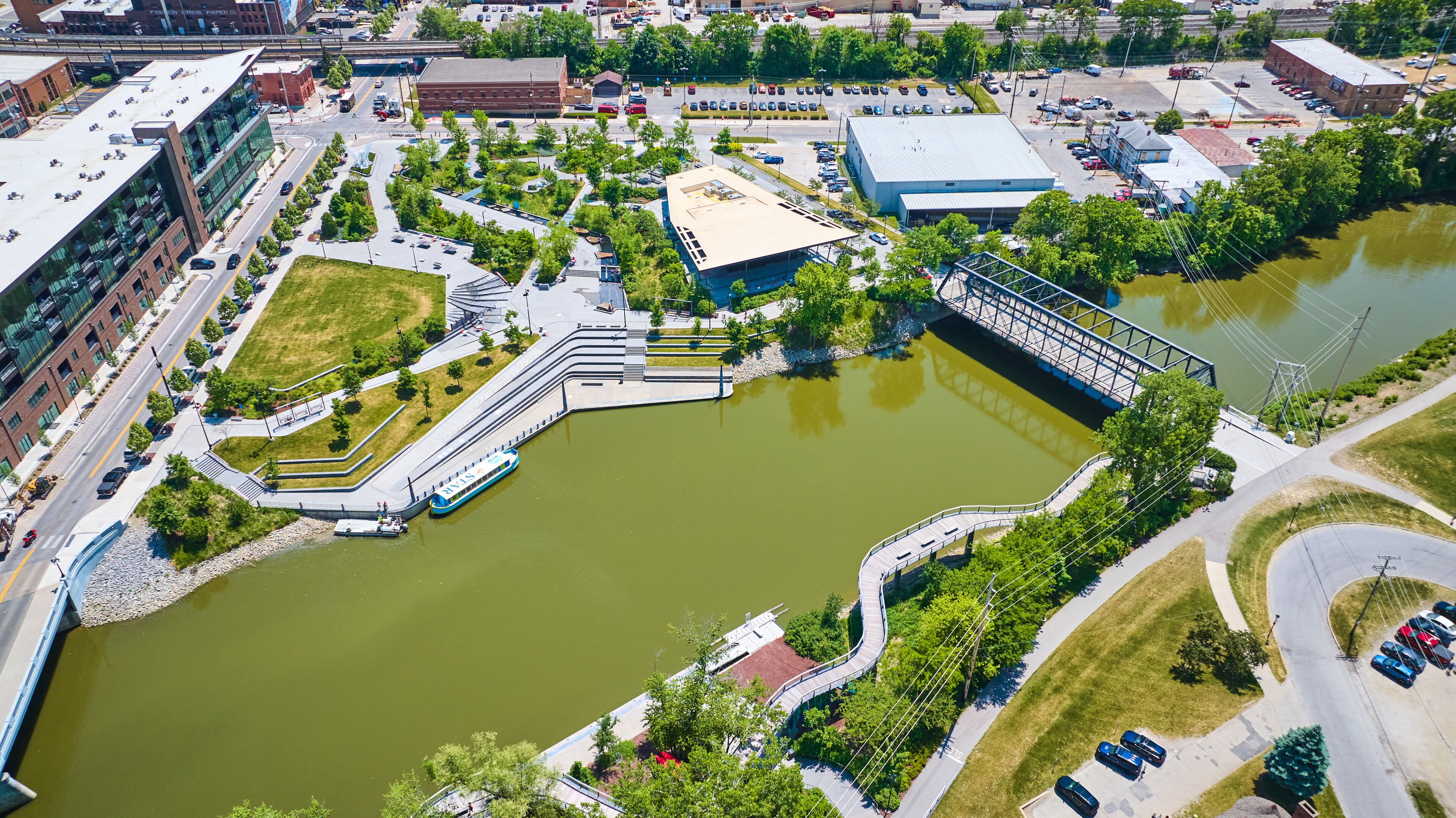 Vista aérea de un paisaje urbano con un parque verde extenso, un puente y un río.