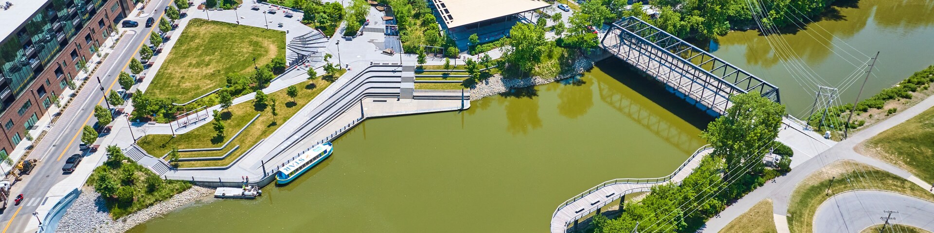 Vista aérea de un paisaje urbano con un parque verde extenso, un puente y un río.