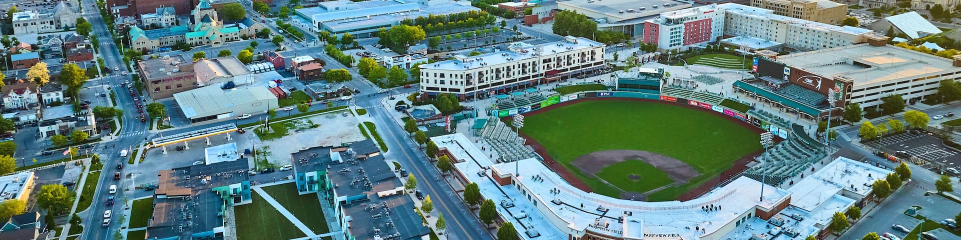 A cityscape with a baseball stadium, commercial buildings, and a river in the background.