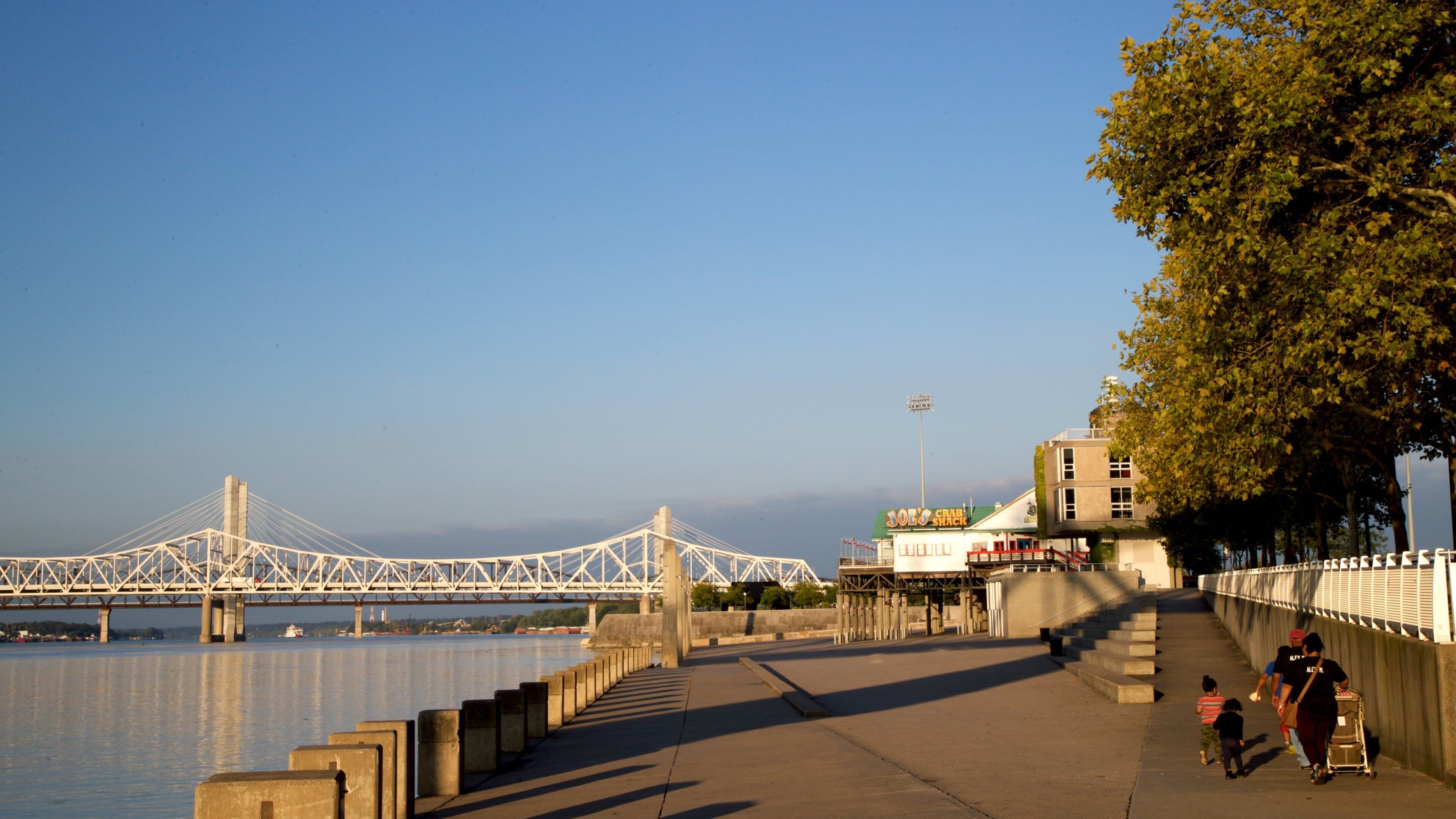 A river with a bridge, a waterfront restaurant, and a pedestrian walkway.
