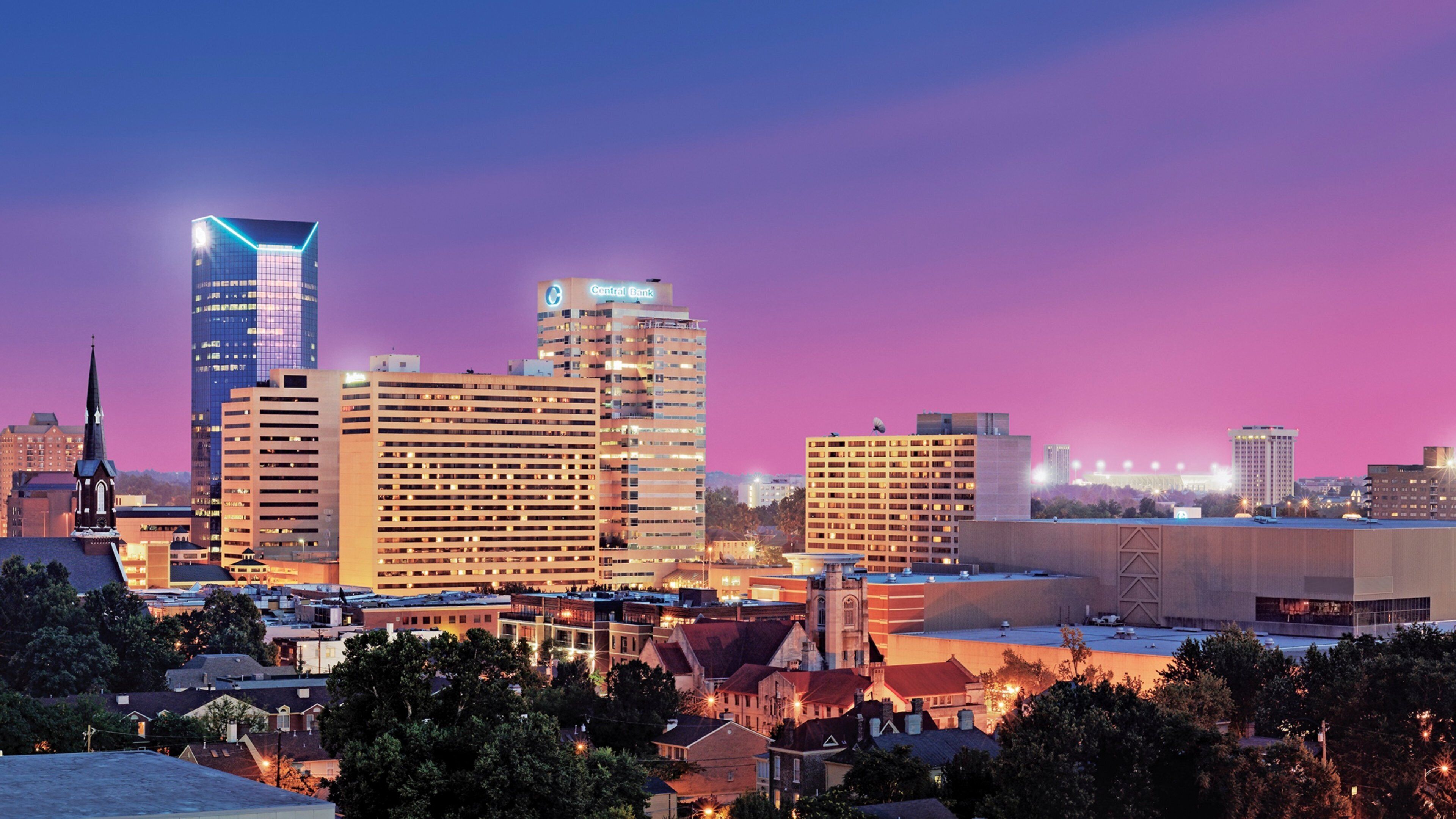 A city skyline with illuminated buildings and a church spire.