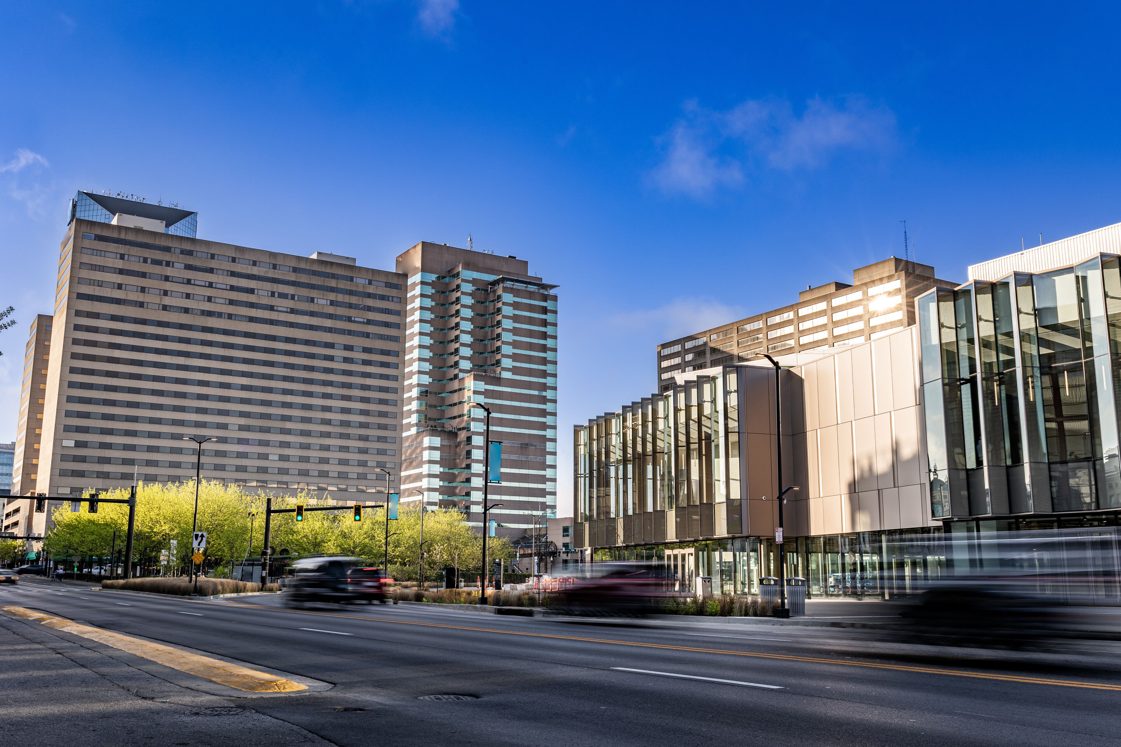 A city street with tall buildings, traffic lights, and a clear blue sky.