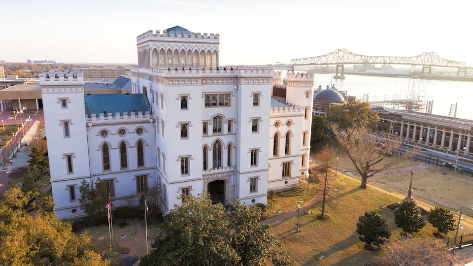 A large white building with a blue roof and a bridge in the background.