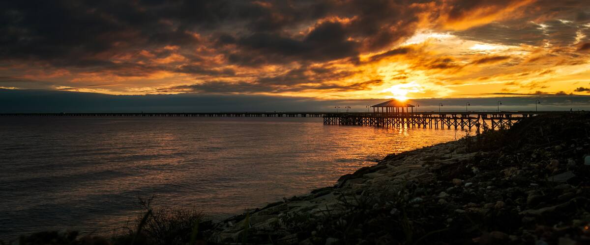 A sunset over a body of water with a pier extending into the distance.