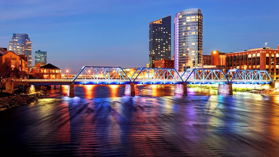 A brightly lit bridge over a river with reflections of city buildings and lights.