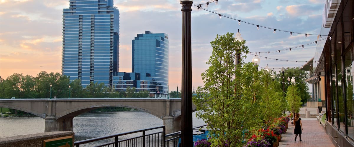 A riverside walkway with a bridge, modern buildings, and string lights.