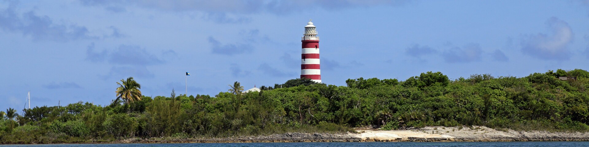 Um farol numa pequena ilha, com águas azuis cristalinas e uma praia de areia.