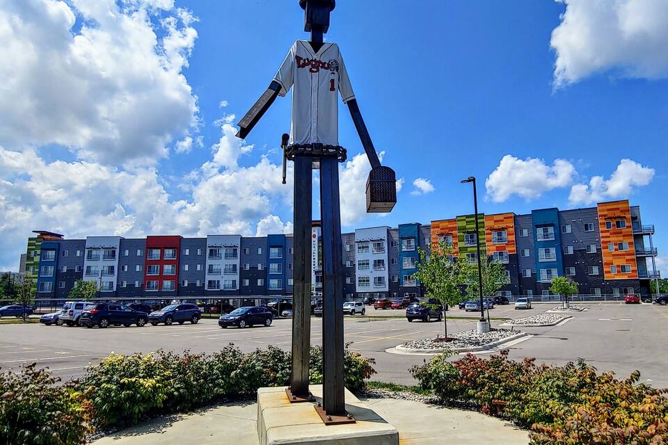 A baseball statue in a plaza with colorful buildings in the background.