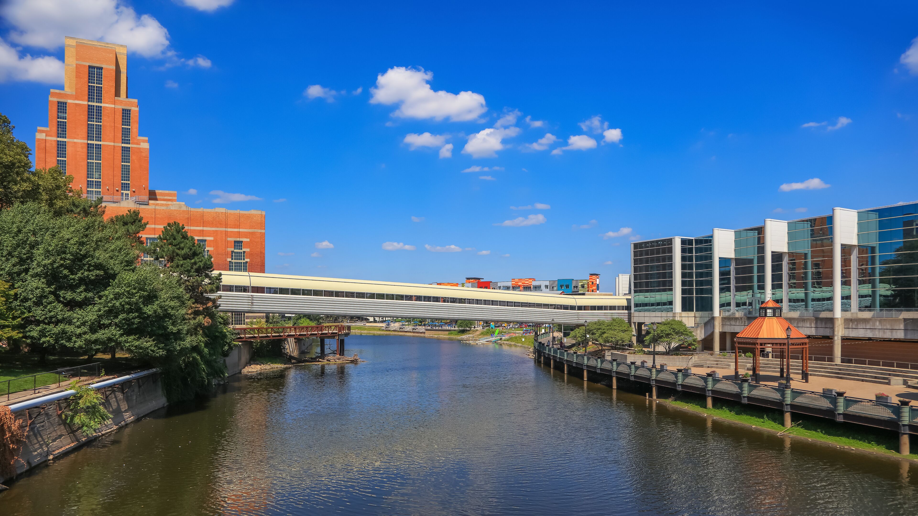 A river with a bridge, a red brick building, and modern glass buildings.