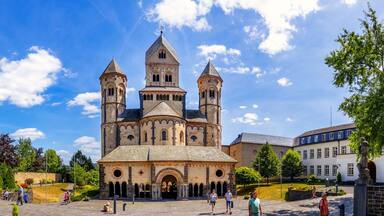 A historic cathedral with two towers, surrounded by a park with trees and people.