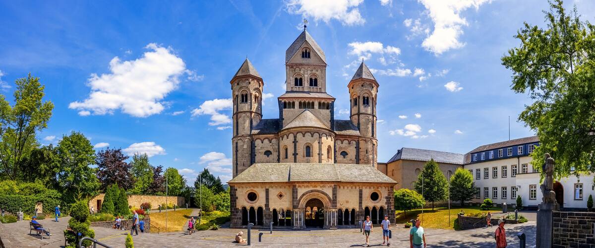 A historic cathedral with two towers, surrounded by a park with trees and people.