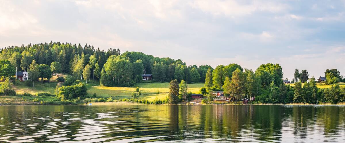A calm lake with reflections of trees and houses on the shore.