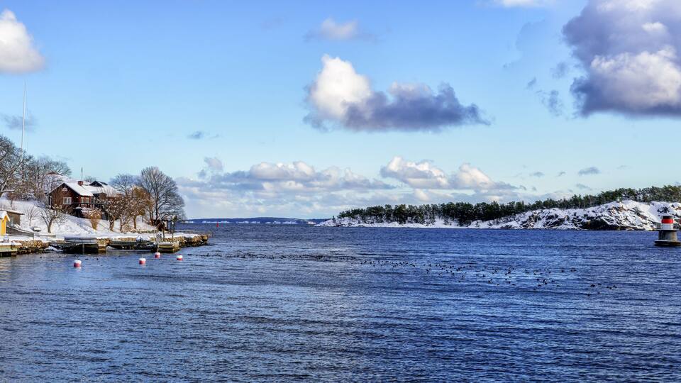 A snowy waterfront with docks, a lighthouse, and a snow-covered island in the distance.