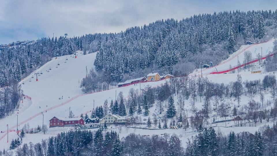 A snowy mountain landscape with ski slopes, a ski lift, and a red-roofed building.
