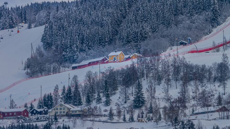 A snow-covered mountain with ski lifts, a red barn, and a yellow house.
