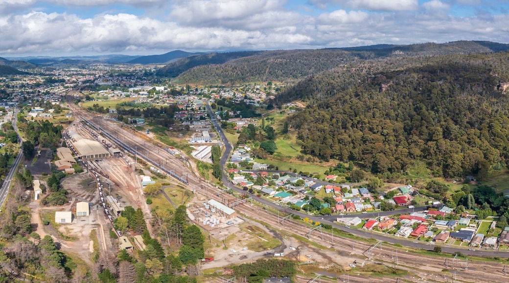 Vista aérea de un pueblo con vías de tren, rodeado de colinas boscosas.