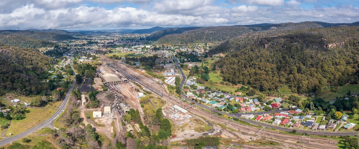 An aerial view of a town with railway tracks, surrounded by forested hills.
