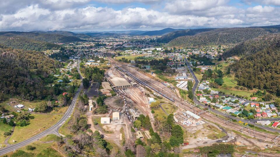 An aerial view of a town with railway tracks, surrounded by forested hills.