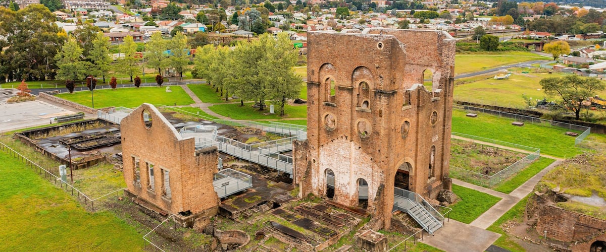 Vista aérea de una torre de ladrillo histórica con una escalera, rodeada por un parque y una zona residencial con casas y árboles.