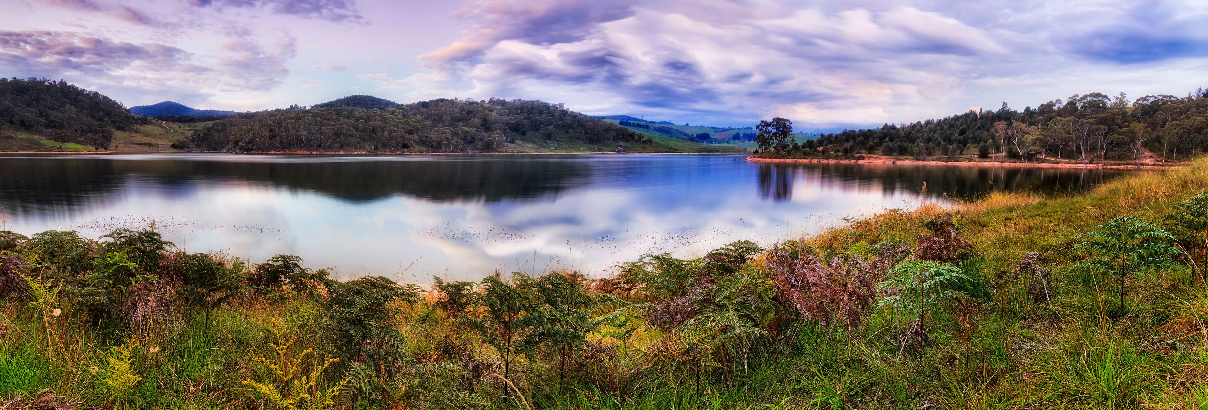 A calm lake surrounded by lush greenery and hills.