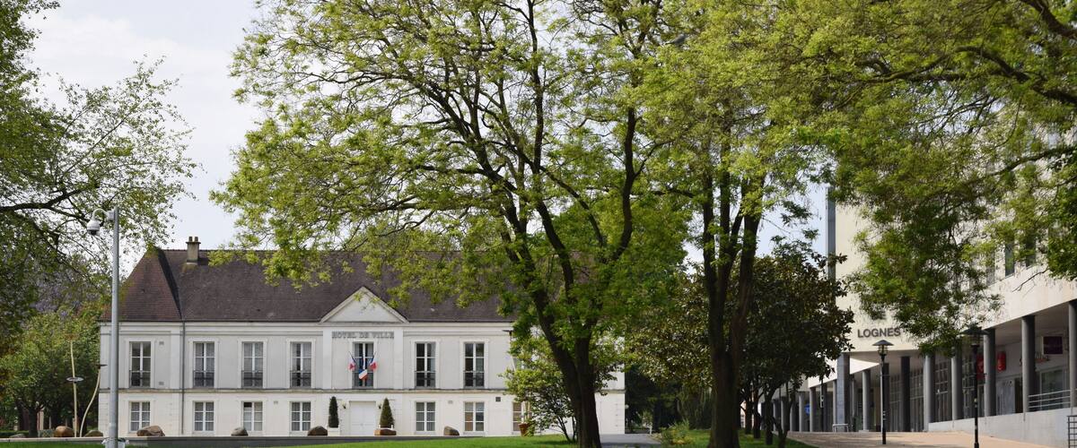 A large white building with a flag, surrounded by trees and a grassy area.