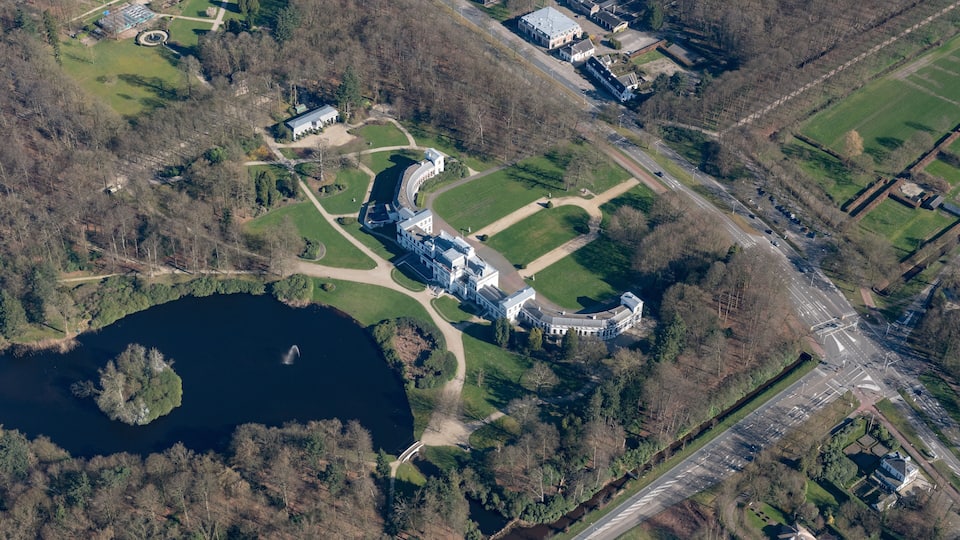 An aerial view of a large estate with a lake, green lawns, and a winding road.