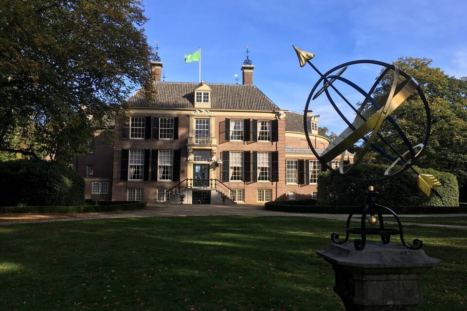 A large brick building with a flag, surrounded by a well-maintained lawn and trees.