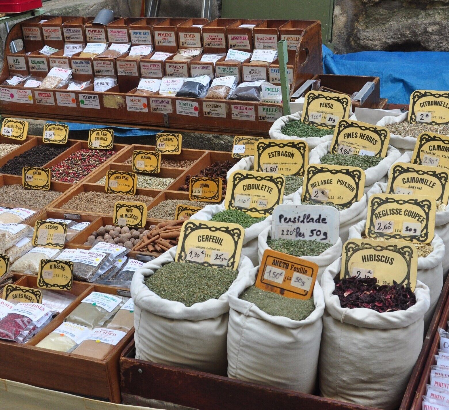 A spice market with various herbs and spices displayed in wooden boxes and sacks.