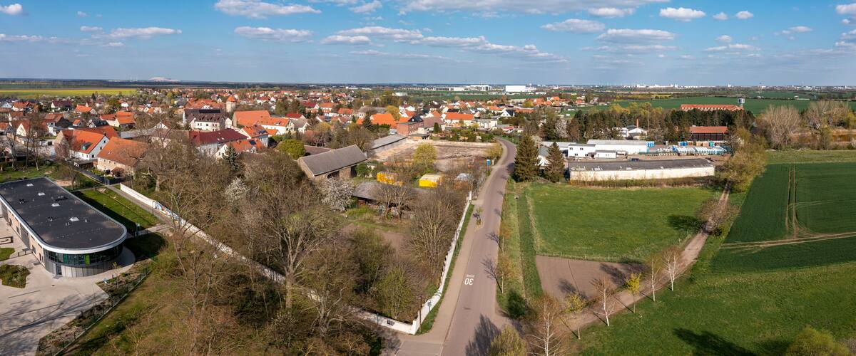 A town with red-roofed houses, a large open field, and a road curving through the landscape.