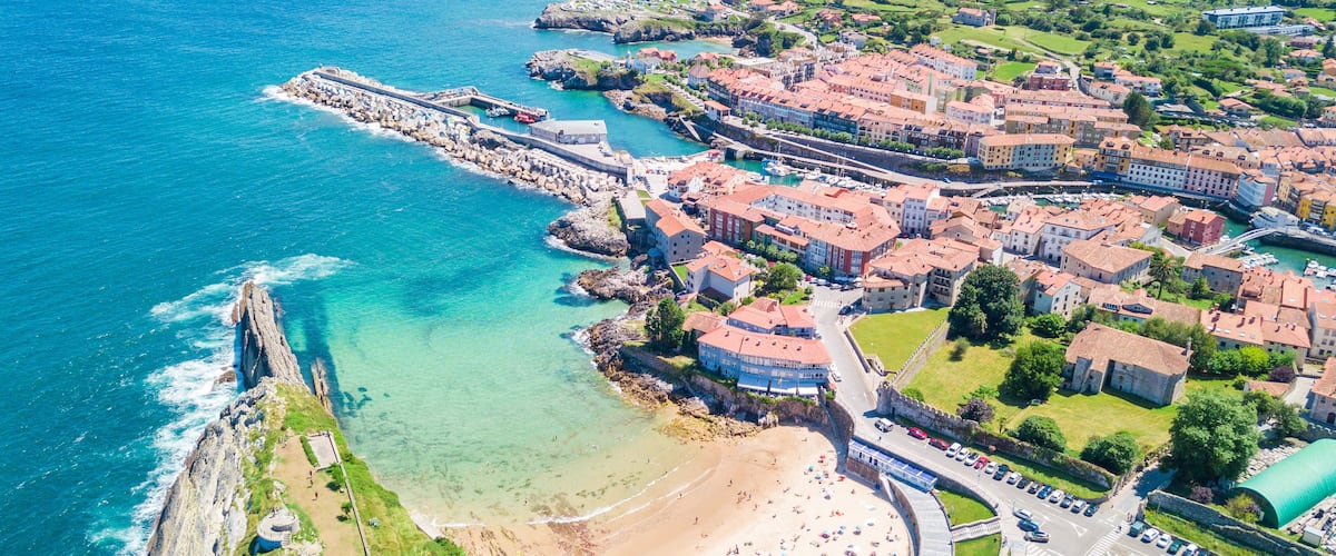 A coastal town with a beach, a fortified harbor, and surrounding greenery.