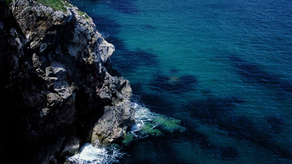 A coastal landscape with rocky cliffs and a clear blue sea.
