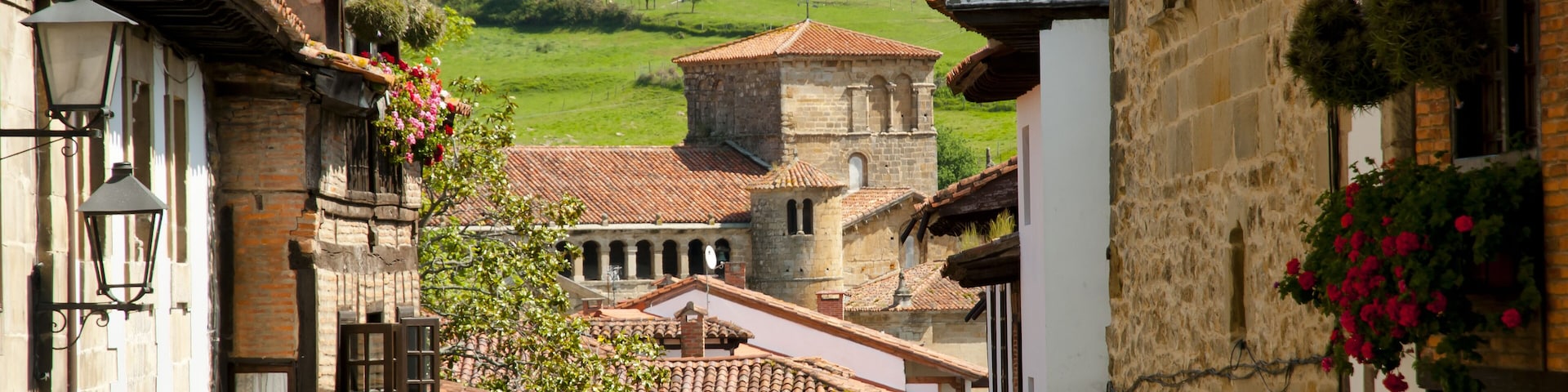 Una calle estrecha con edificios tradicionales, una torre y una ladera verde al fondo.