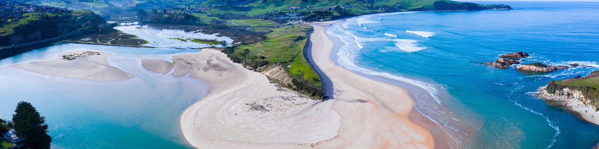 A coastal landscape with a sandy beach, a river mouth, and green hills in the background.