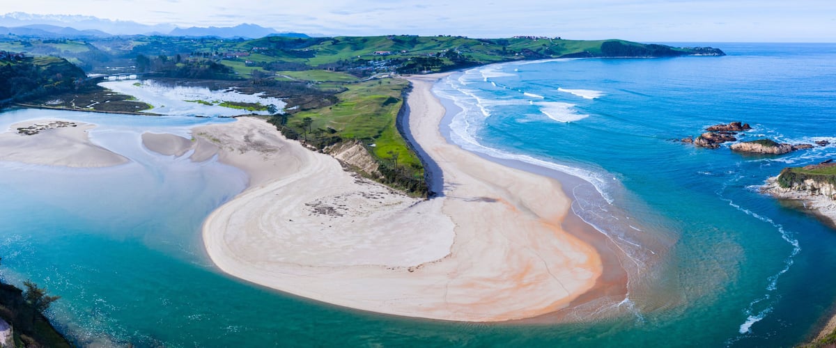 A coastal landscape with a sandy beach, a river mouth, and green hills in the background.