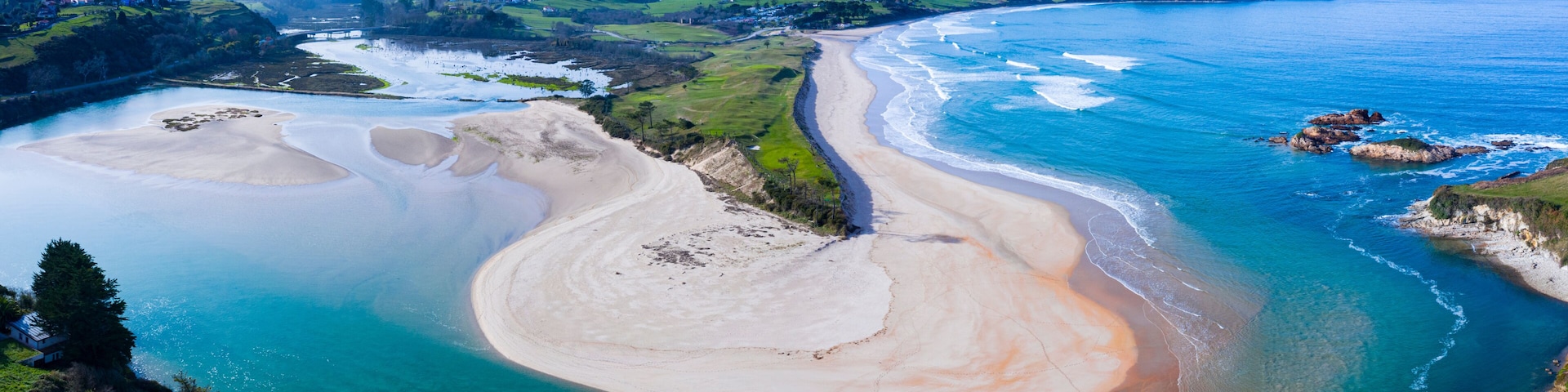 A coastal landscape with a sandy beach, a river mouth, and green hills in the background.