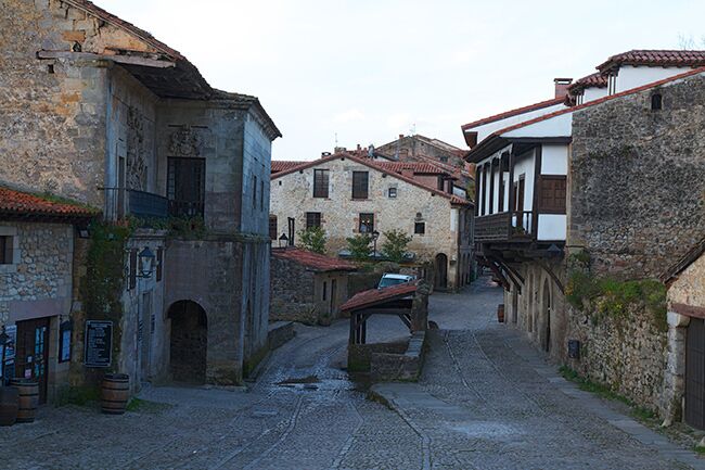 A narrow cobblestone street in a historic town with old stone buildings and a small bridge.