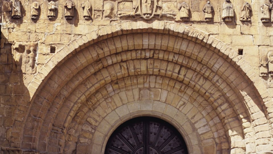 A historic stone building with a large arched doorway, columns, and detailed carvings.