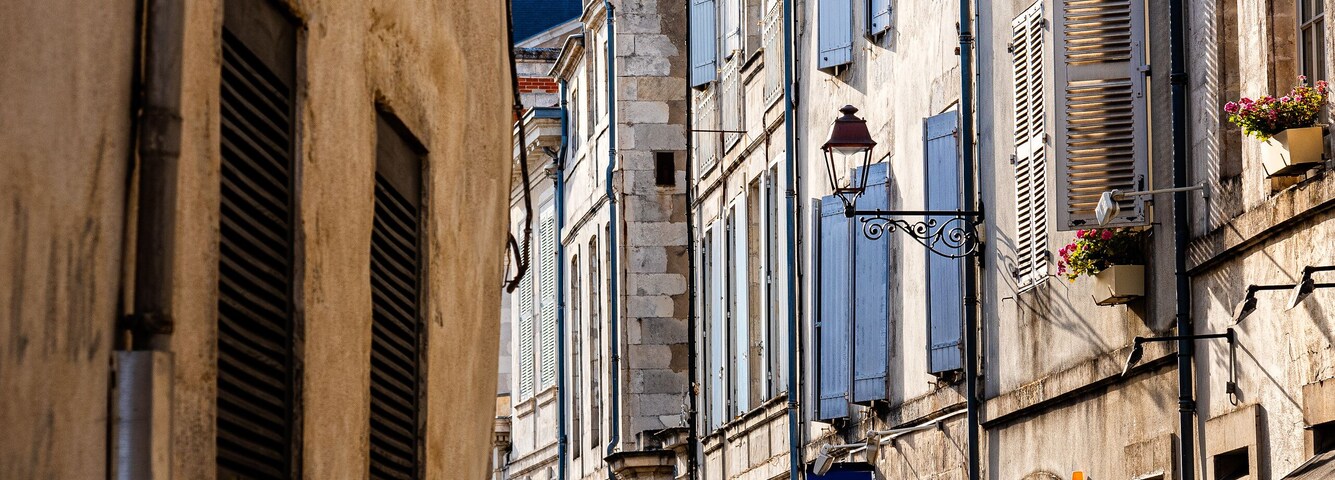 A narrow street lined with old buildings, shutters, and a street lamp.