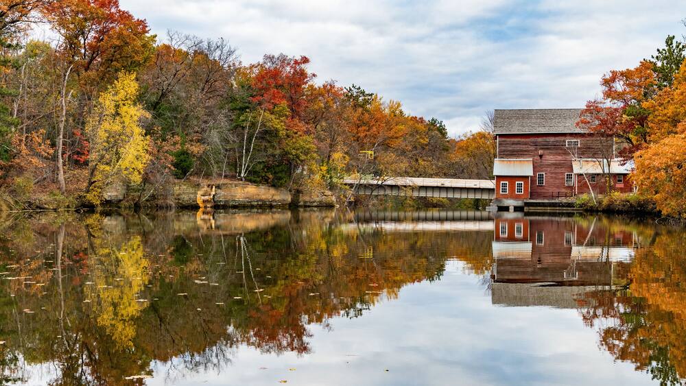 A wooden building by a calm river with autumn foliage.